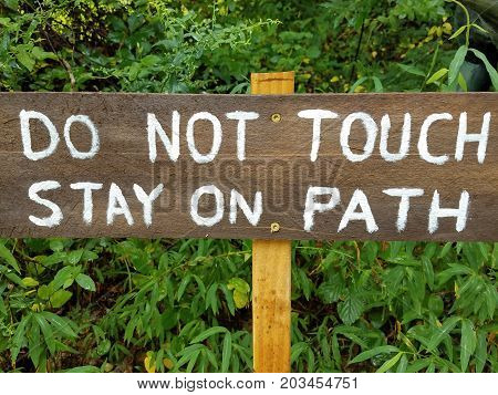 a wood do not touch stay on path sign with plants