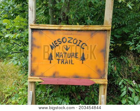 an orange wooden mesozoic nature trail sign and green plants