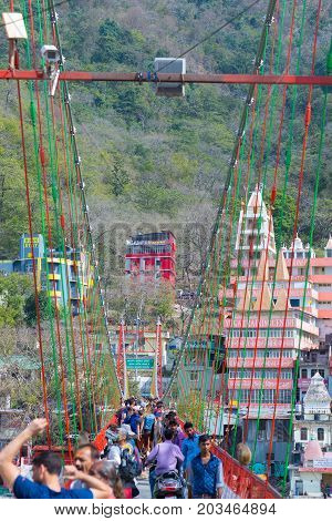 Rishikesh, India - March 10, 2017: People Crossing The Ganges River On The Suspension Footbridge At