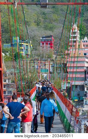 Rishikesh, India - March 10, 2017: People Crossing The Ganges River On The Suspension Footbridge At