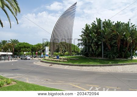 CAMBRILS, SPAIN - AUG 27th, 2017: Modern sculpture A tota vela, a round about and the main street promenade in the port area with Cambrils sign in the background.