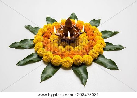 flower rangoli for Diwali or pongal or onam made using marigold or zendu flowers and red rose petals over white background with diwali diya in the middle, selective focus