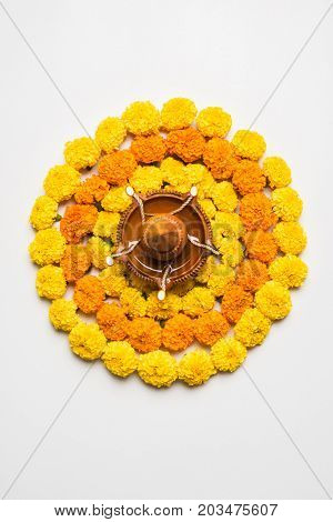 flower rangoli for Diwali or pongal or onam made using marigold or zendu flowers and red rose petals over white background with diwali diya in the middle, selective focus