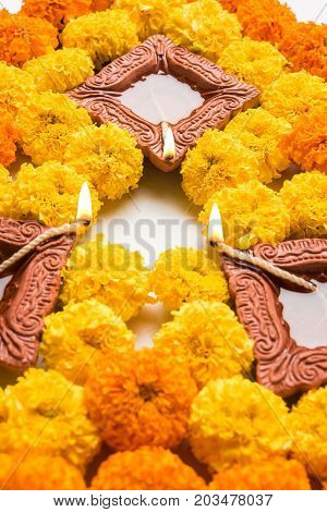 flower rangoli for Diwali or pongal or onam made using marigold or zendu flowers and red rose petals over white background with diwali diya in the middle, selective focus