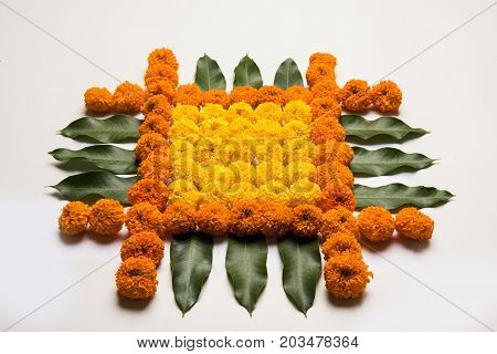 flower rangoli for Diwali or pongal or onam made using marigold or zendu flowers and red rose petals over white background with diwali diya in the middle, selective focus
