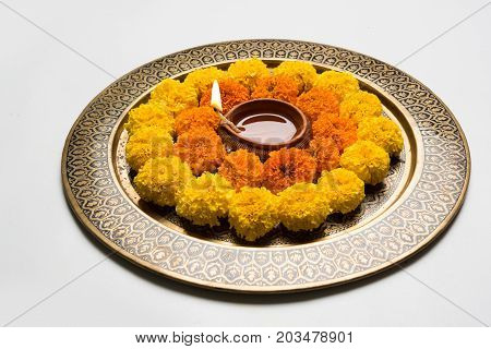 flower rangoli for Diwali or pongal or onam made using marigold or zendu flowers and red rose petals over white background with diwali diya in the middle, selective focus