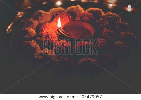 flower rangoli for Diwali or pongal or onam made using marigold or zendu flowers and red rose petals over white background with diwali diya in the middle, selective focus