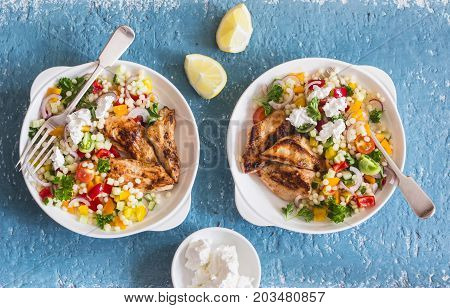 Yogurt marinated grilled chicken breast and israeli couscous and vegetables tabouli salad on a blue background top view