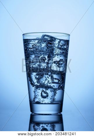 glass of water with ice cubes on a light blue background with reflection
