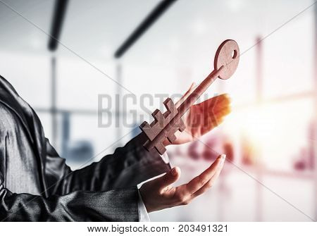 Business woman in black suit keeping big stone key in hands with office view and sunlight on background. Mixed media.