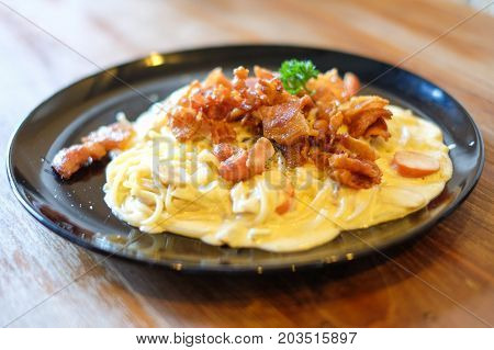 The spaghetti carbonara with bacon and mushroom cream sauce on black dish set on brown wooden table for food background or texture - homemade food concept.