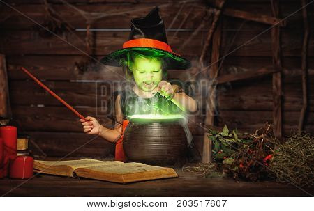 Halloween. little witch child cooking potion in the cauldron with spell book