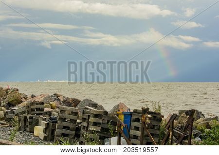 garbage on the shore of the reservoir river sea ocean on the horizon in the sunlight city and rainbow