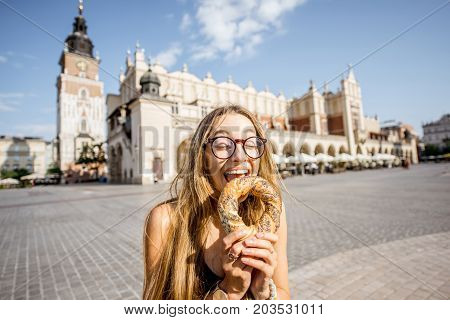 Young woman tourist eating prezel on the market square in Krakow in Poland
