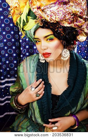 beauty bright woman with creative bright make up, many shawls on head like cubian, ethno look closeup