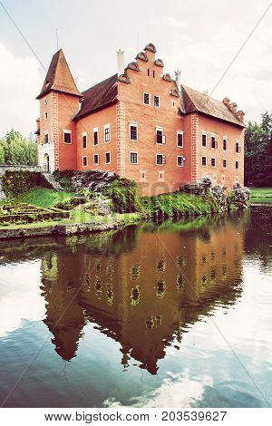 Cervena Lhota is a beautiful chateau in Czech republic. It stands at the middle of a lake on a rocky island. Retro photo filter. Mirrored architecture.