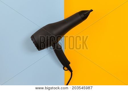 Black hair dryer on blue and yellow paper background. Top view. Copy space. Flat lay. Still life. Mockup