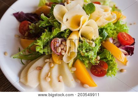 Lettuce salad with cheese and fruits on plate. Fresh vegetables decorated pine nuts, avocado, pearch and pear, serving in restaurant, close up picture