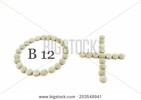 Contour of a circle and the plus sign made up of spirulina pills with word B12 inside. Supplement of vitamin B12. White background.