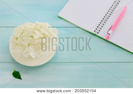 Open notebook with pink pen coffeecup and hydrangea on mint wooden background. Copy space background