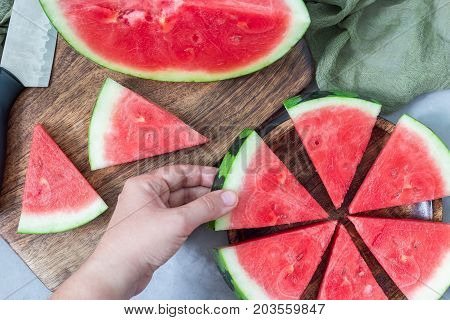 Woman hand take a slice of fresh seedless watermelon cut into triangle shape laying on a wooden plate flat lay horizontal