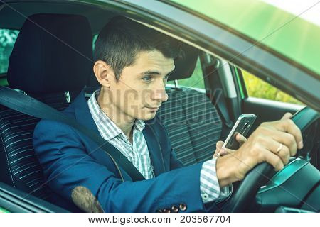 Driver Man Looking At Phone In Car. Distracted And Dangerous Driving. The Traffic Violation.