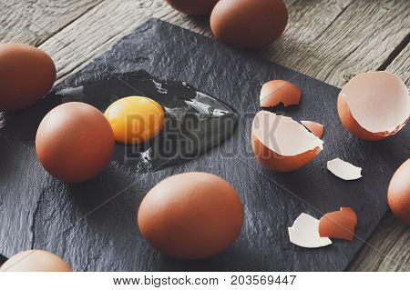 Fresh chicken brown home eggs with cracked eggshell and yolk on rustic slate black background. Closeup. Natural healthy food and organic cooking ingredients