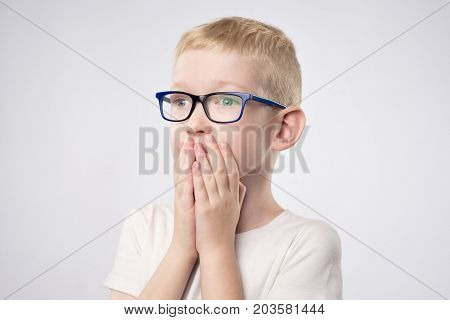 Scared litle kid boy with blond hair holding hands on face because he is afraid. Concept of negative emotion