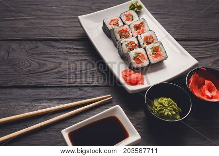 Eating rolls at sushi restaurant. Japanese food, maki on dark background. Set with soy, gignger and chopsticks. Closeup on black wood