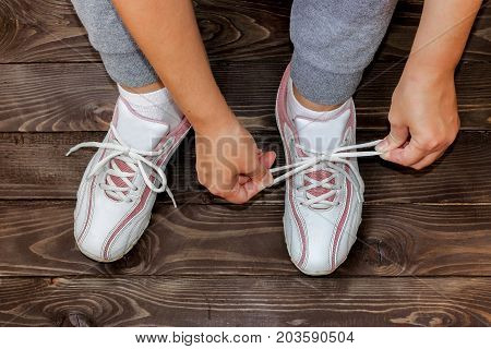 Tying Shoe laces girl sitting on the wooden floor. White sneakers on a dark wooden background.The view from the top.