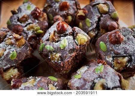 Pieces Of Homemade Chocolate Brownie Cake With Nuts, Bananas, Coconut And Sugar Powder  On A Wooden