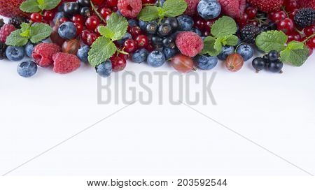 Various fresh summer berries on white background. Ripe raspberries blueberries blackberries gooseberries black currants and red currants mint. Berries at border of image with copy space for text. Background berries. Top view.