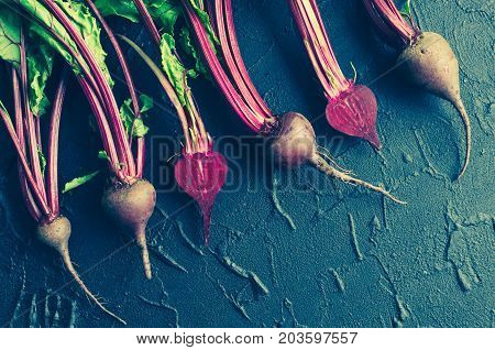 Row of homegrown organic young beets with green leaves on dark stone table. Food background. Concept of healthy eating. Toned image. Top view. Copy space.