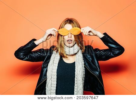 Season and autumn holiday. Beauty and fashion. Girl with orange leaves. Woman with autumn leaves as glasses in leather jacket. surprised model with stylish hair in scarf.