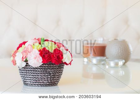 Colorful carnations in brown vase and candle on marble table.