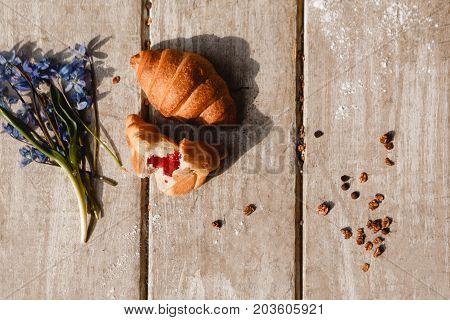Delicious breakfast on wooden background. Sweet croissant and granola with spring blue snowdrops nearby. Morning fresh and tasty meal. Food photography top view