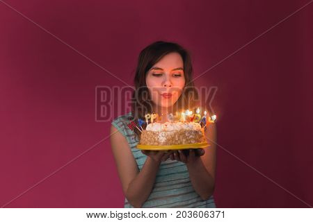 Young woman blowing out candles on a birthday cake over gray background
