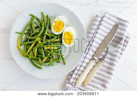 Cooked green beans with boiled eggs in white plate. Healthy vegetarian food concept. Top view.