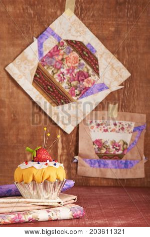 The pin cushion like a cupcake with strawberry and patchwork blocks of the cup and the teapot with a pattern of flowers hanging on wall