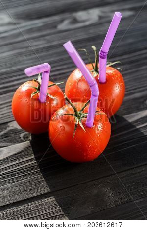 Three Ripe Red Tomatoes with Straws on Black Wooden Table Close-up. Fresh Juice Healthy Food Concept. Tomato as a Vessel with Fresh Juice