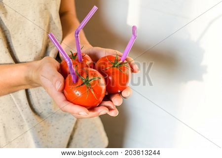 Three Ripe Red Tomatoes with Straws in Woman Hands on Bright Background. Fresh Juice Healthy Food Concept. Tomato as a Vessel with Fresh Juice