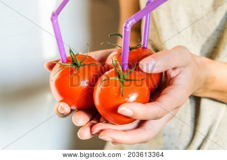 Three Ripe Red Tomatoes with Straws in Woman Hands on Bright Background. Fresh Juice Healthy Food Concept. Tomato as a Vessel with Fresh Juice