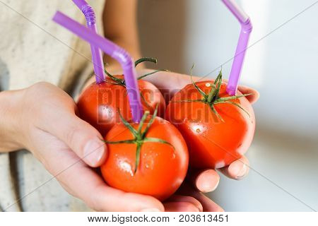 Three Ripe Red Tomatoes with Straws in Woman Hands on Bright Background. Fresh Juice Healthy Food Concept. Tomato as a Vessel with Fresh Juice