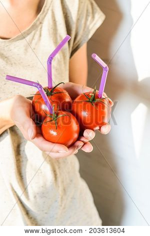 Three Ripe Red Tomatoes with Straws in Woman Hands on Bright Background. Fresh Juice Healthy Food Concept. Tomato as a Vessel with Fresh Juice