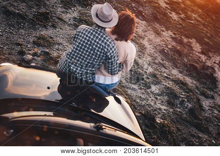 Loving Couple Sits On Hood Convertible Car And Enjoy View At Sunset. Young Trendy Hipsters Near Cabr