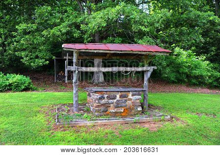 Old fashioned water well is covered and abandoned. Frayed rope is wound around log ar across tope of well. Well is in Northern Arkansas.