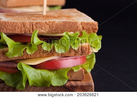 Close-up Big Sandwich With Ham, Cheese, Tomatoes And Salad On Toasted Bread On A Dark Background
