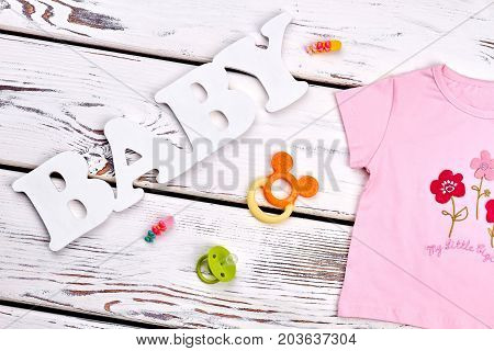 Baby-girl brand apparel, accessories. Infant girl cute cotton t-shirt, teether, pacifier, hair accessories on old wooden background. Infant baby background.