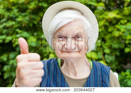 Elderly woman with mental disorder showing thumbs up in the park