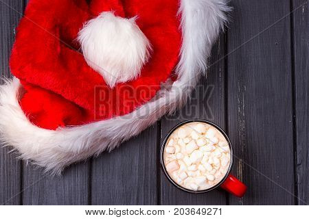 Hot chocolate with marshmallows and cap santa on grunge dark table